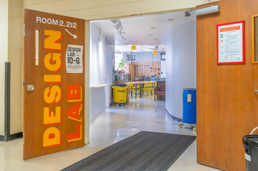 The open doors of the Design Lab, looking down the entrance corridor. The wooden doors have large yellow and orange text that reads Design Lab.