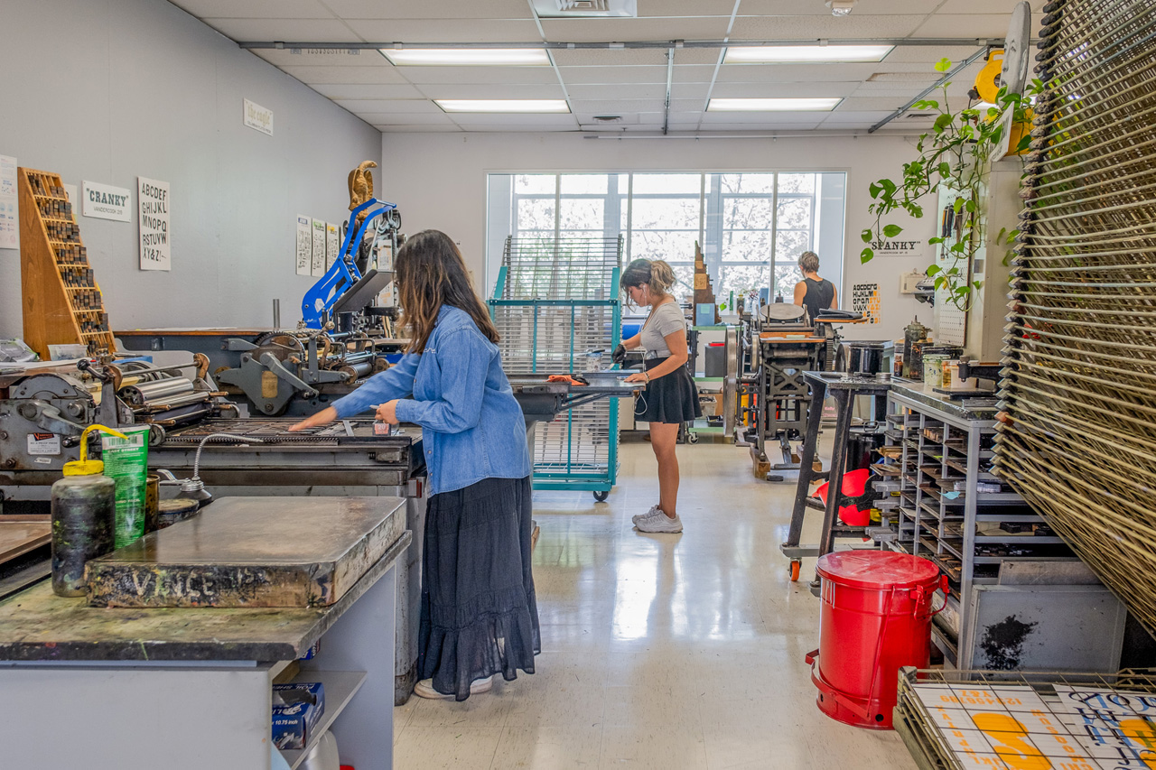 student residency employees work at each of the antique presses in the UT Design Lab