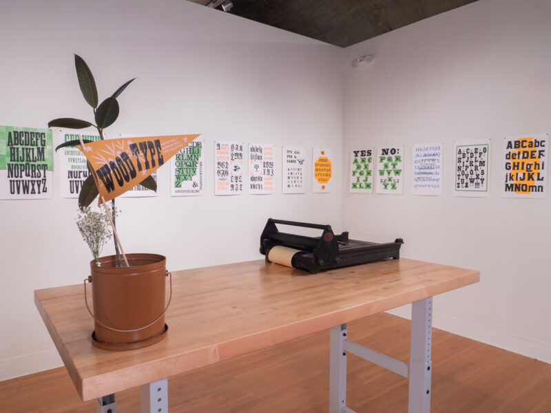 installation of RRK Folio Specimen Revisited prints on wall at the Visual Arts Center at UT Austin, tabletop press and plant in foreground