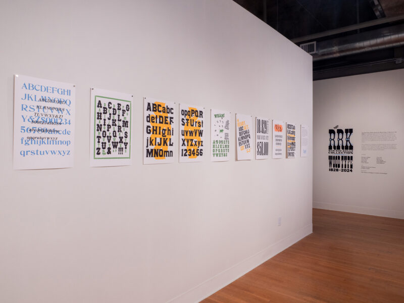 installation of RRK Folio Revisited Specimen prints on wall at the Visual Arts Center at UT Austin, gallery entrance in background