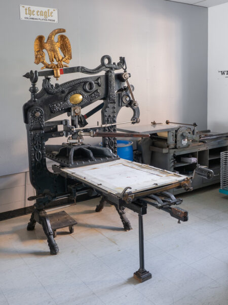The press has a white name plaque mounted to the gray wall above it, reading Vinny.