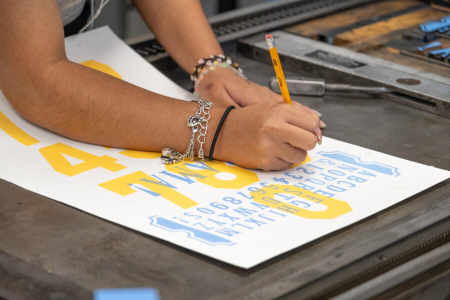 A student using a pencil to make annotations on a print, on the pressbed of the Vandercook 219