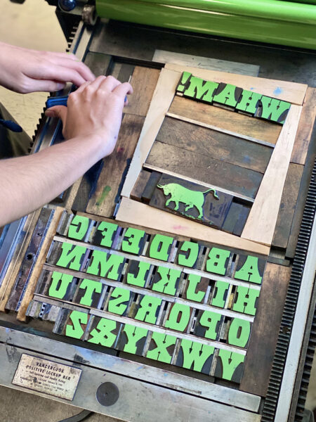 A student working on a lockup on the SP15 pressbed. Wood type is secured with custom furniture, and is coated with green ink.
