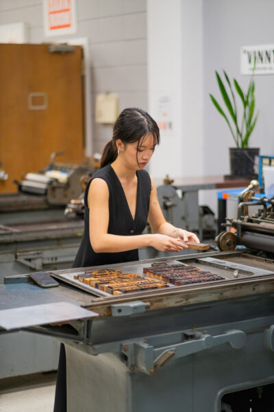 A student organizing wood type on a tray sitting on the Vandercook 219 pressbed.